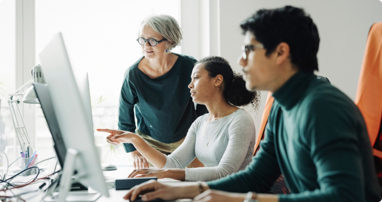 Three employees in an office environment. Two women are discussing something on screen.