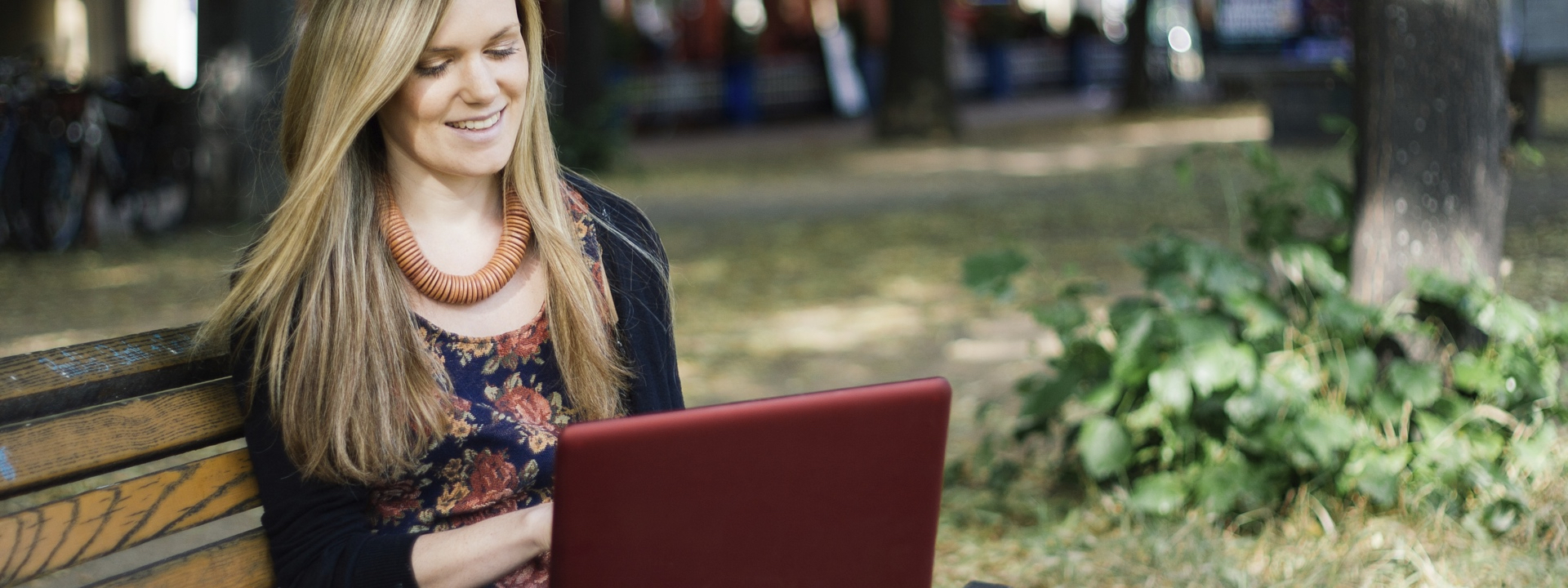 Young blonde woman in a park bench with a red laptop computer